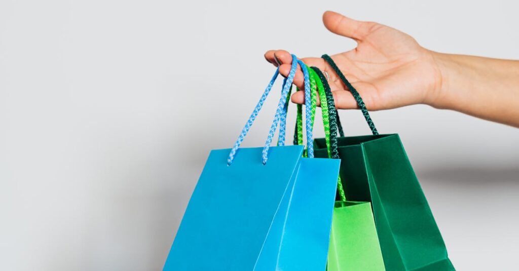 Hand holding three colorful paper shopping bags on a white background.